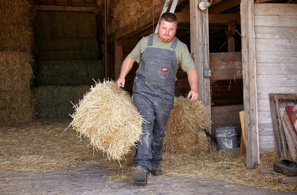 Man in a barn carrying a bundle of hay
